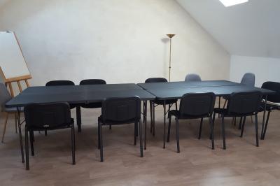 Salle de réunion avec tables noires, chaises, écran de projection, tableau blanc et éclairage naturel.