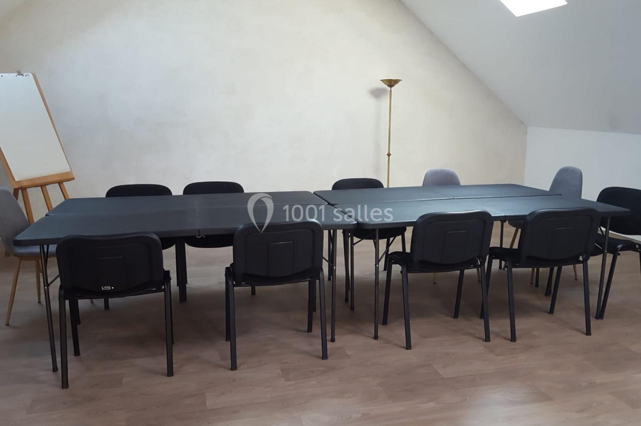 Salle de réunion avec deux grandes tables noires, plusieurs chaises, un tableau chevalet et un lampadaire.