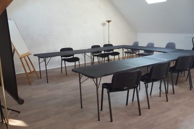 Salle de réunion avec tables noires, chaises, écran de projection, tableau blanc et éclairage naturel.