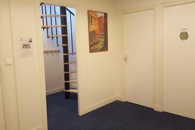 Salle de réunion avec tables noires, chaises, écran de projection, tableau blanc et éclairage naturel.