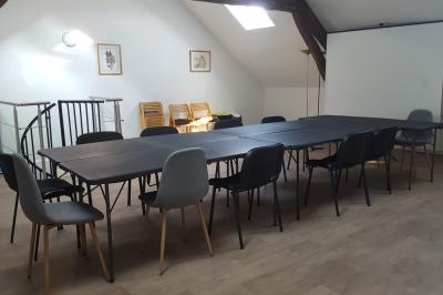 Salle de réunion avec tables noires, chaises, écran de projection, tableau blanc et éclairage naturel.