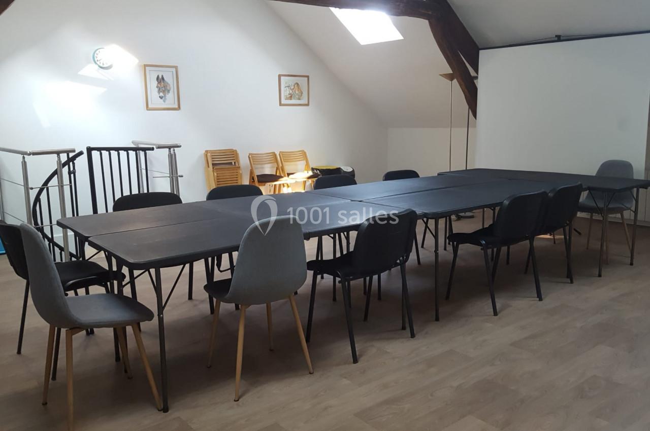 Salle de réunion lumineuse avec tables noires alignées, chaises variées et écran de projection en arrière-plan.