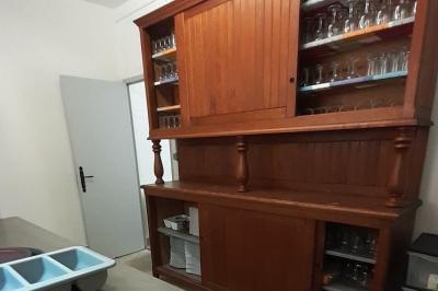 Cuisine professionnelle avec plans de travail en inox, réfrigérateur blanc, étagères murales et sol en carrelage.