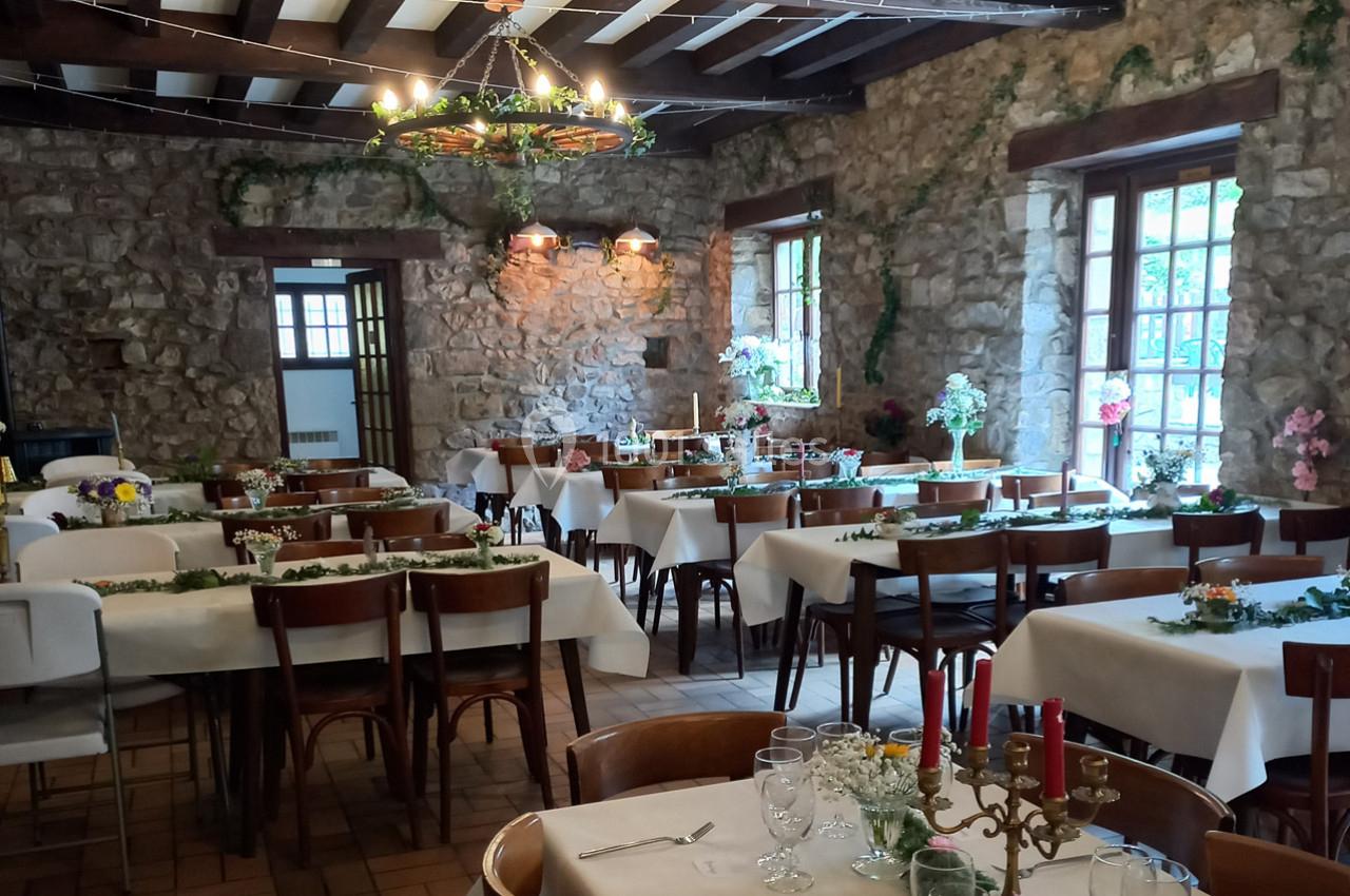 Salle de réception rustique avec murs en pierre, tables dressées avec nappes blanches et décorations florales.