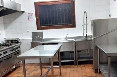 Cuisine professionnelle avec plans de travail en inox, réfrigérateur blanc, étagères murales et sol en carrelage.