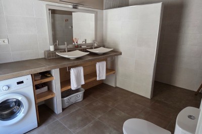 Salle de bain moderne avec douche à l'italienne, paroi vitrée, meuble vasque blanc et carrelage beige et marron.