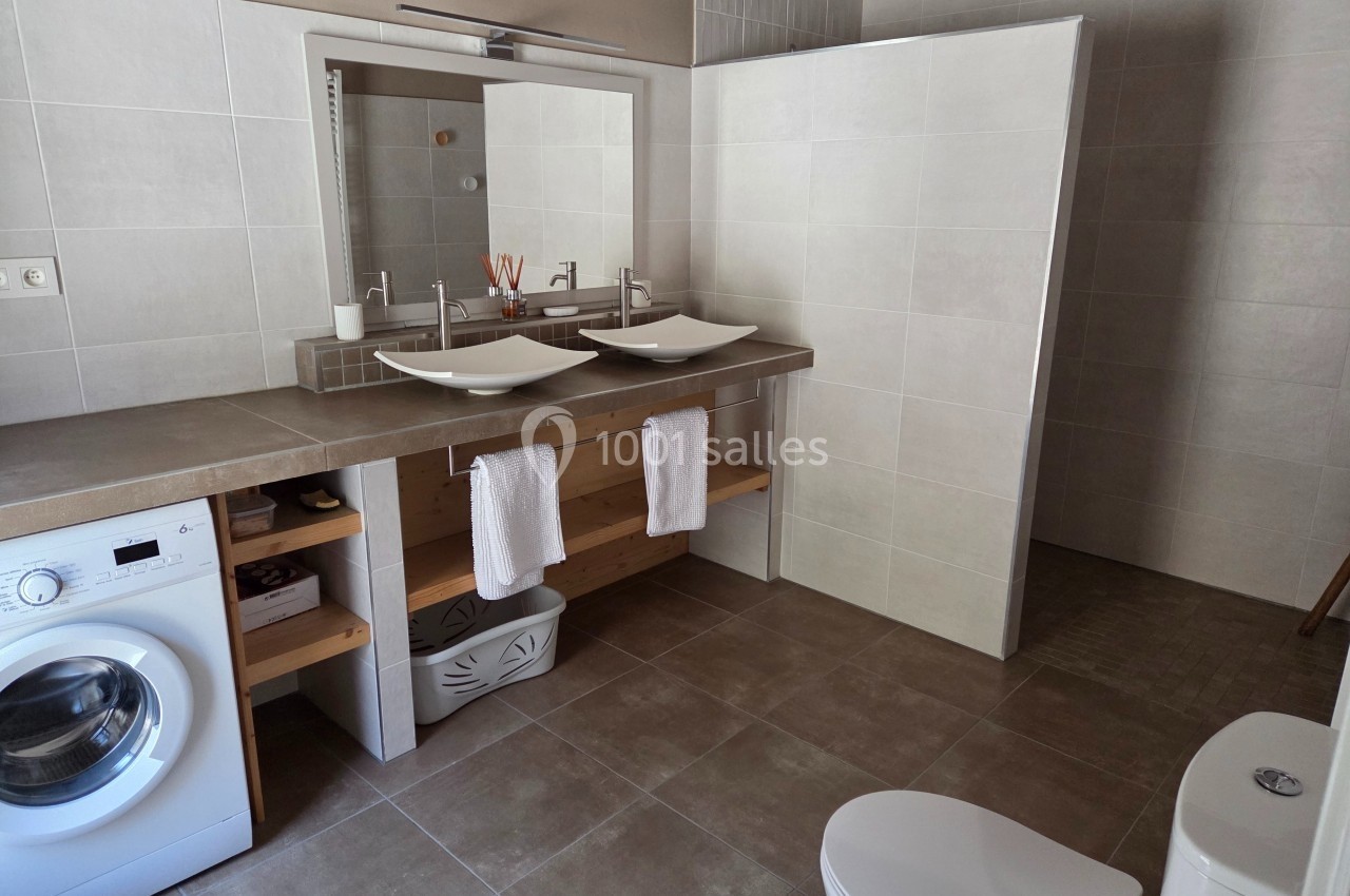 Salle de bain moderne avec double vasque, douche à l'italienne, lave-linge et toilettes sur carrelage beige.