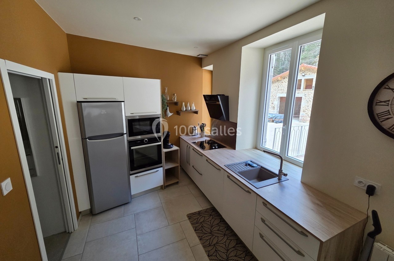 Cuisine moderne avec réfrigérateur, four, plaques de cuisson, évier et rangements, éclairée par une fenêtre.