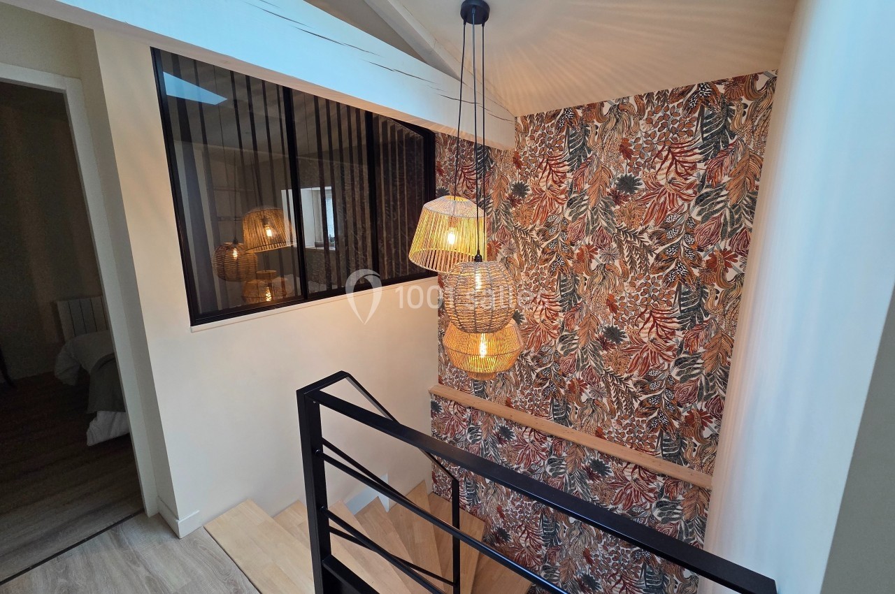 Escalier moderne avec garde-corps noir, suspension lumineuse et mur décoré d’un papier peint à motifs végétaux.