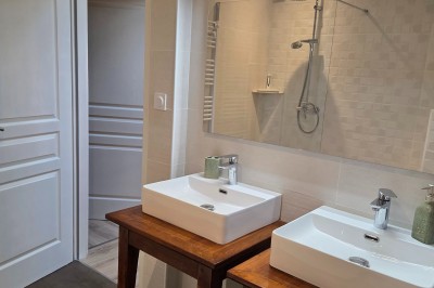 Salle de bain moderne avec douche à l'italienne, paroi vitrée, meuble vasque blanc et carrelage beige et marron.