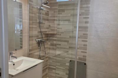 Salle de bain moderne avec douche à l'italienne, paroi vitrée, meuble vasque blanc et carrelage beige et marron.