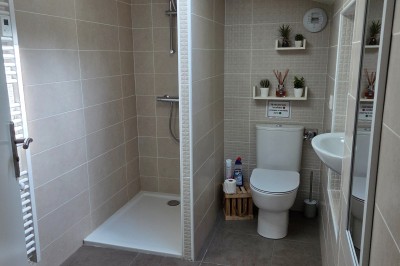 Salle de bain moderne avec douche à l'italienne, paroi vitrée, meuble vasque blanc et carrelage beige et marron.