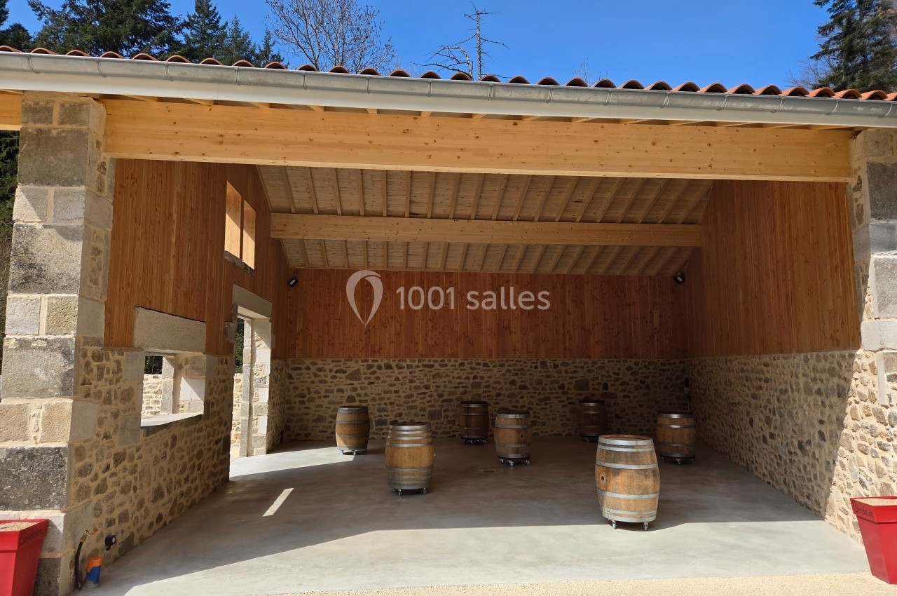 Salle ouverte avec murs en pierre et bois, contenant plusieurs tonneaux en bois sur roulettes, sous un ciel dégagé.