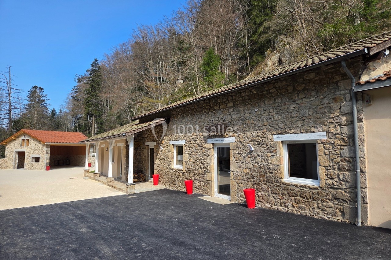 Bâtiments en pierre avec toits en tuiles, entourés de forêt, sous un ciel bleu clair.