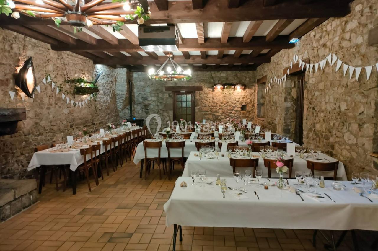 Salle de réception en pierre avec tables dressées pour un repas, décorée de guirlandes et de lustres en bois.