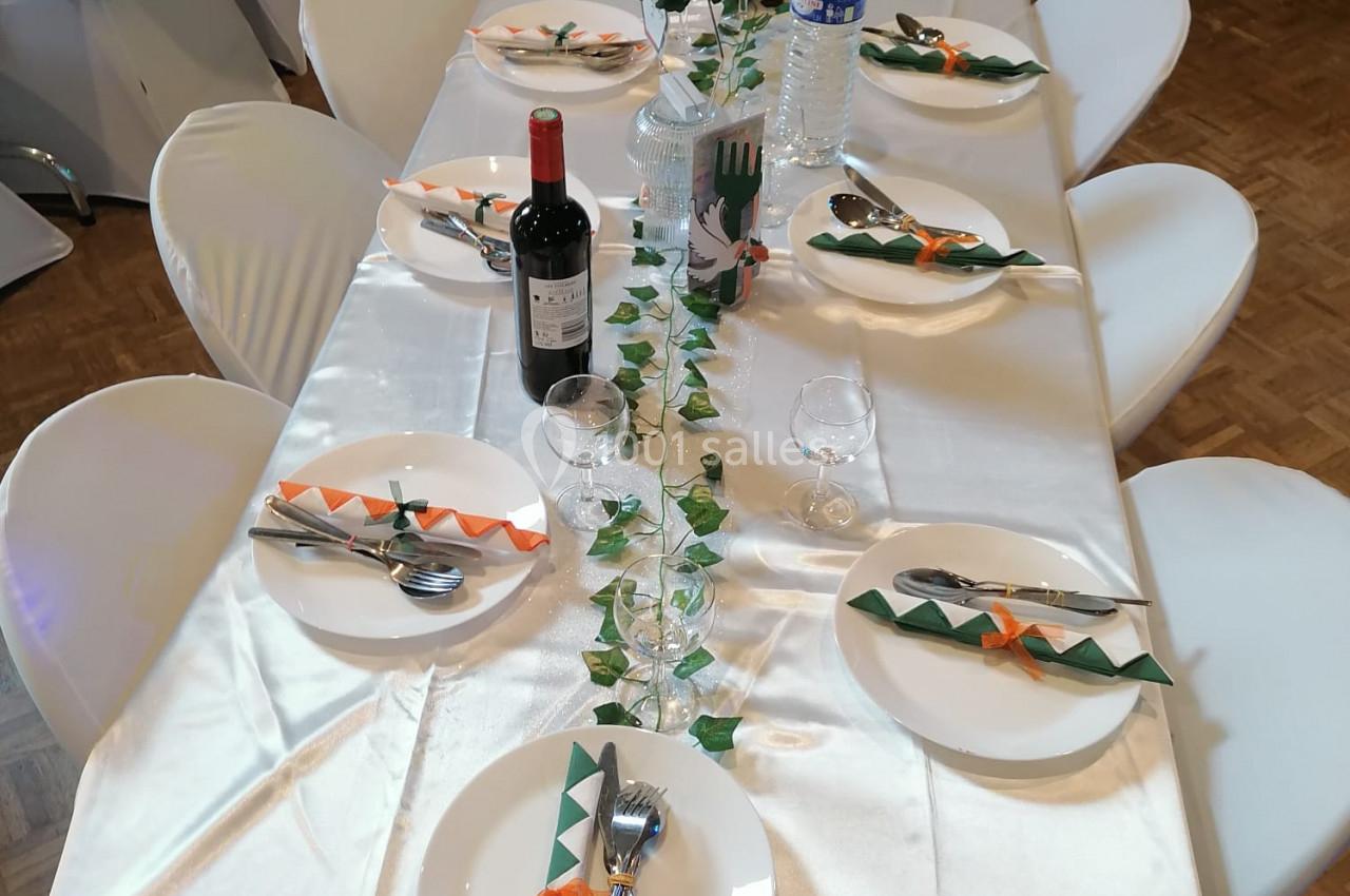 Table dressée avec une nappe blanche, décorée de serviettes vertes et orange, bouteilles, verres et centre de table floral.