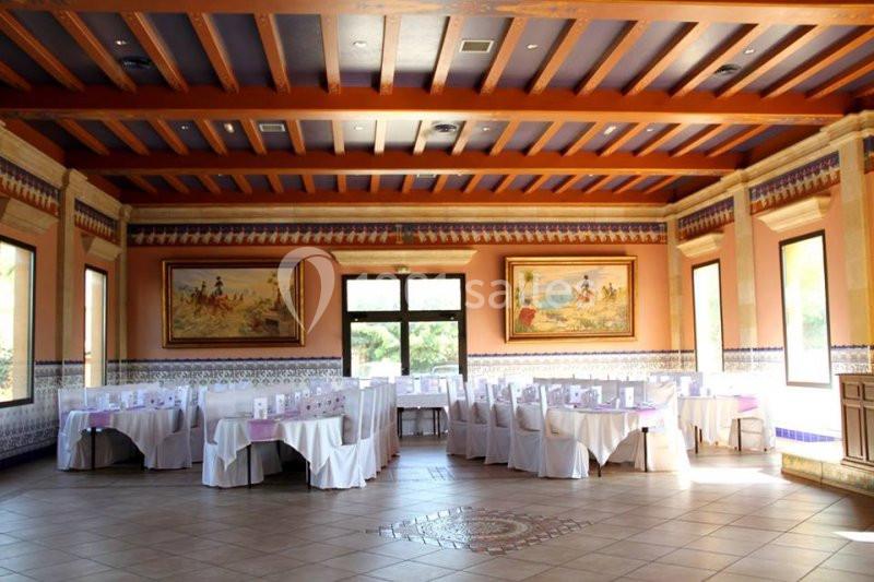 Salle de réception lumineuse avec tables dressées, décorée de fresques murales et de poutres apparentes au plafond.