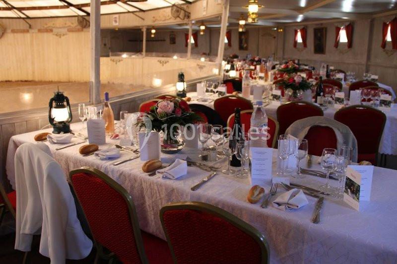 Tables dressées avec nappes blanches, vaisselle élégante, bouquets de fleurs et lanternes dans une salle de réception.