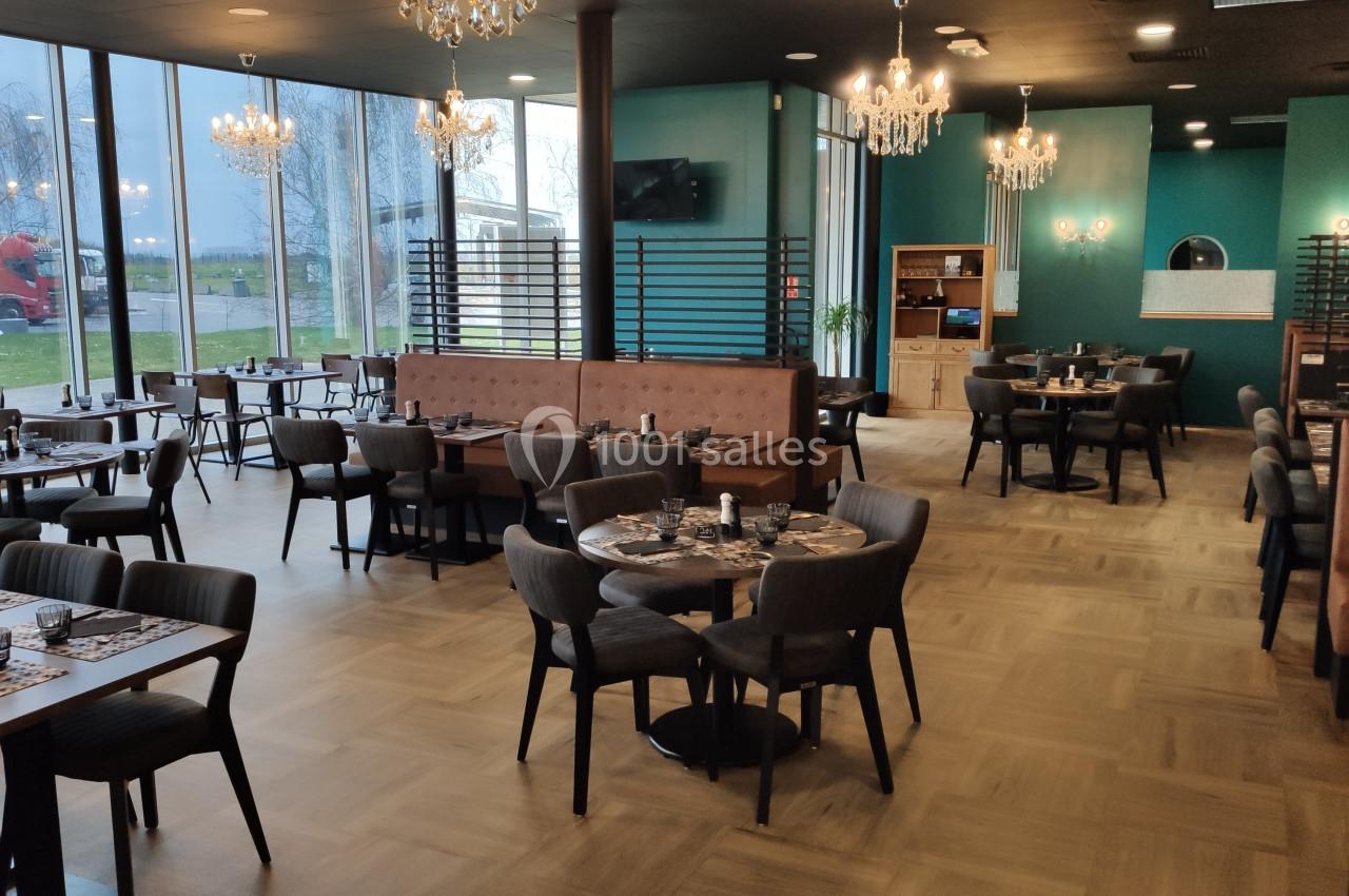 Salle de restaurant moderne avec tables dressées, chaises rembourrées, banquettes et grandes baies vitrées donnant sur l…