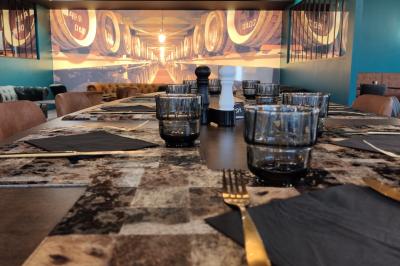 Bar moderne avec comptoir en marbre noir, étagères remplies de verres et bouteilles, machine à café et écran allumé.