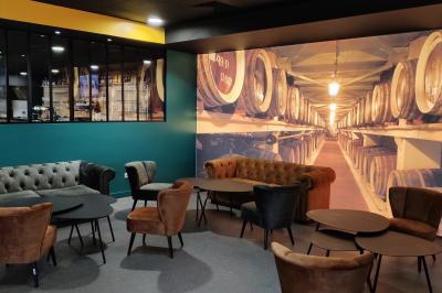 Bar moderne avec comptoir en marbre noir, étagères remplies de verres et bouteilles, machine à café et écran allumé.