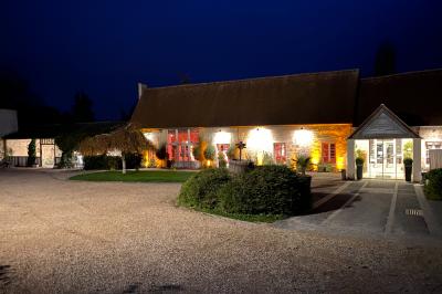 Bâtiment rural éclairé de nuit avec des murs en pierre, des fenêtres rouges et une entrée vitrée sur la droite.