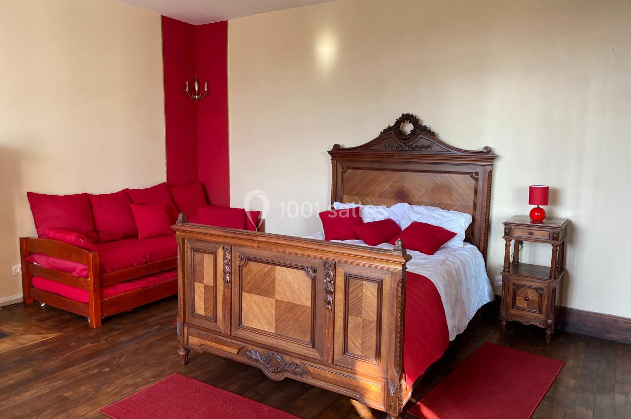 Chambre avec lit en bois sculpté, canapé rouge, lampes assorties et parquet foncé.