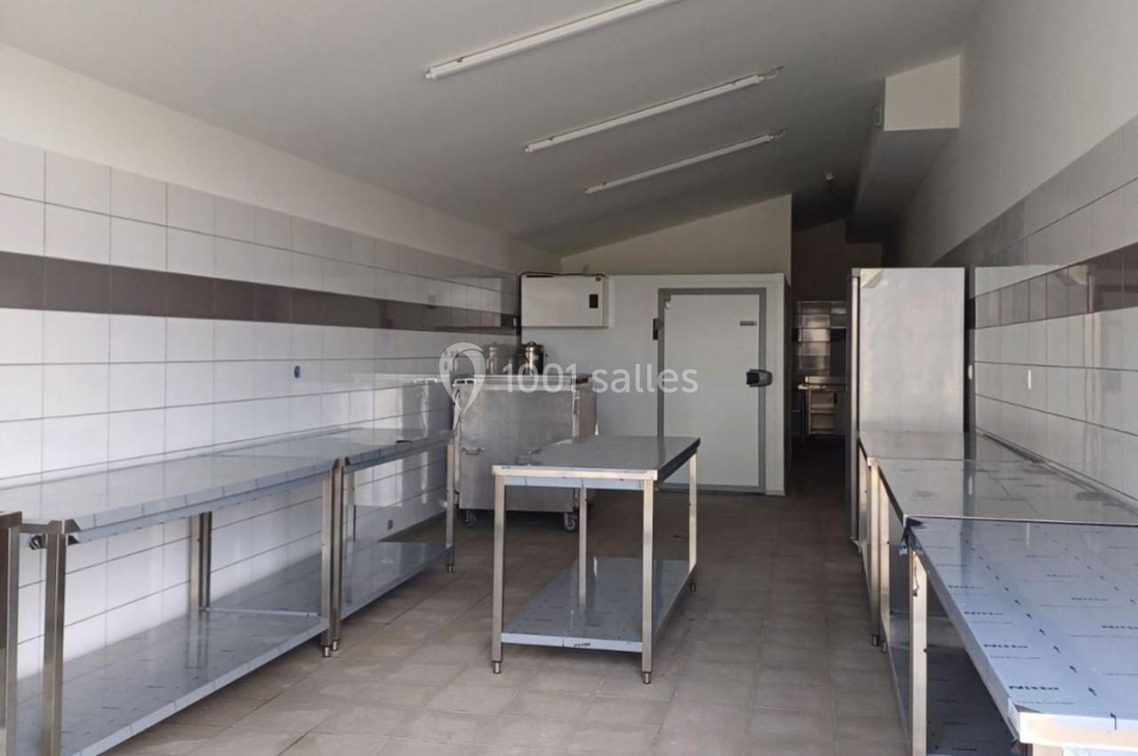 Cuisine professionnelle vide avec plans de travail en inox, murs carrelés blancs et éclairage fluorescent au plafond.