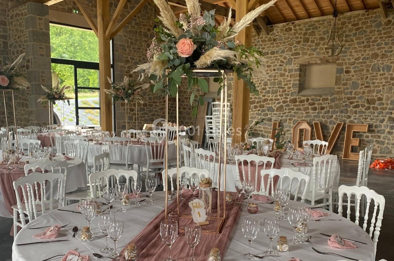Salle de réception décorée pour un mariage avec tables rondes, nappes roses, fleurs et chaises blanches.