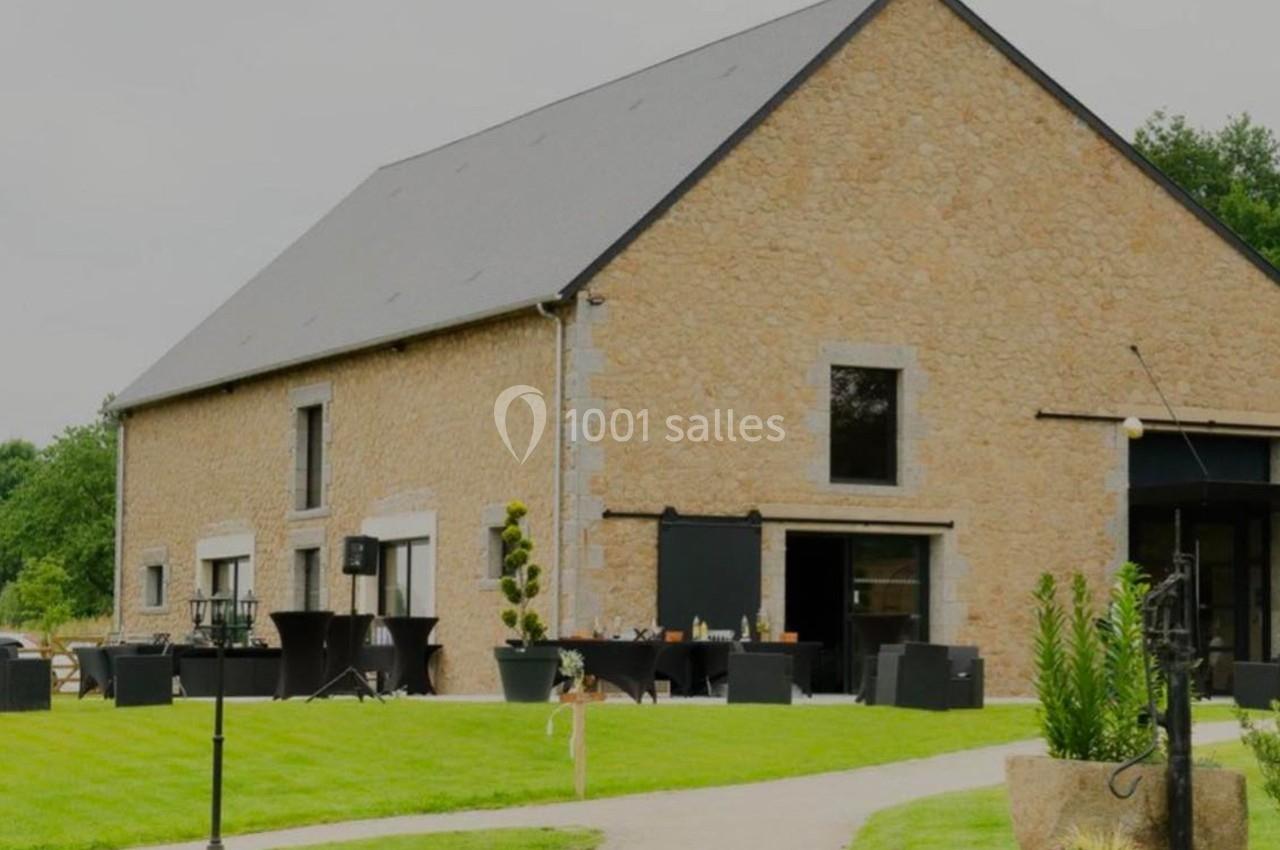 Bâtiment en pierre avec toit en ardoise, entouré d'une pelouse et de mobilier extérieur sur une terrasse.