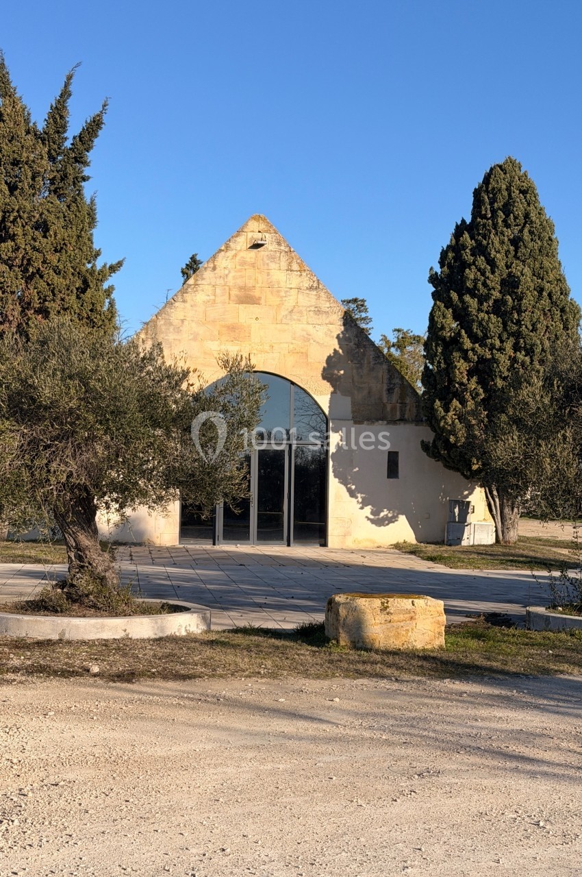 Bâtiment en pierre de style traditionnel avec une grande porte vitrée, entouré d'arbres et d'un espace dégagé.