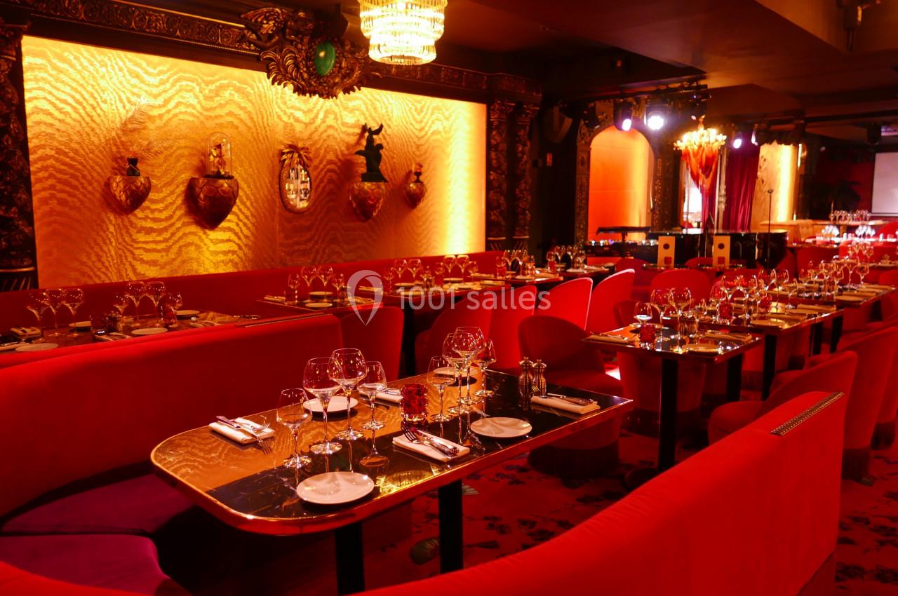 Salle de restaurant élégante avec tables dressées, banquettes rouges, éclairage chaleureux et décorations murales dorées.