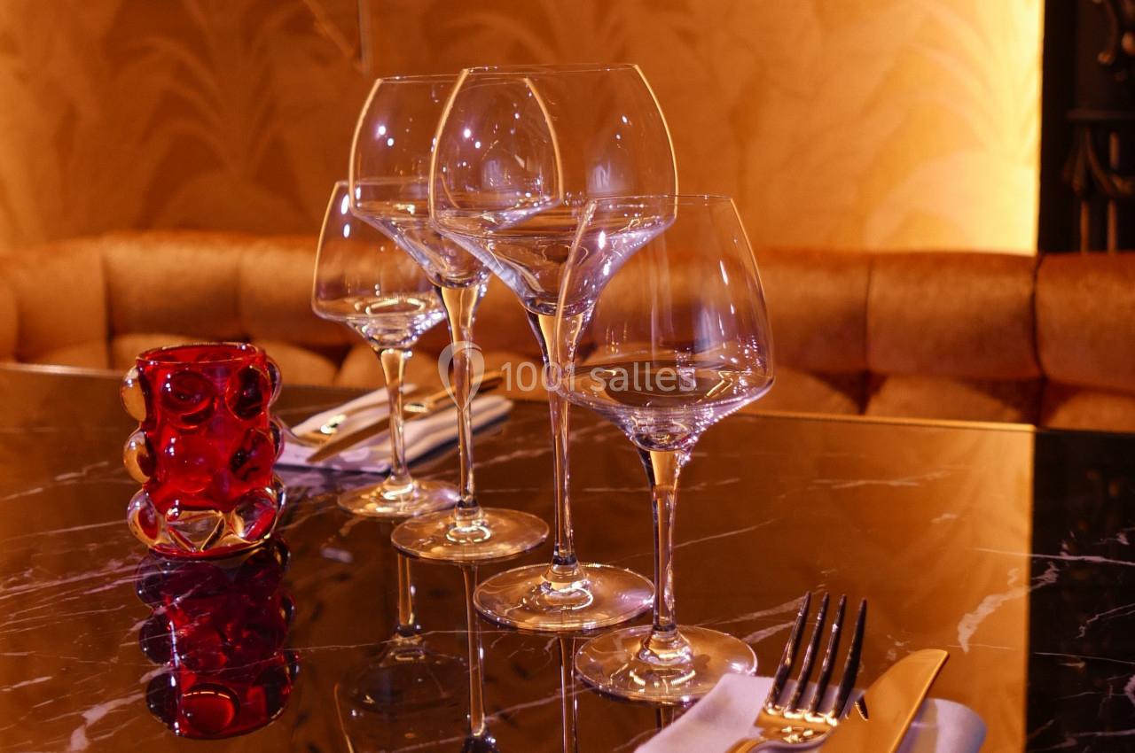 Quatre verres à vin alignés sur une table en marbre noir, avec un photophore rouge et des couverts à proximité.