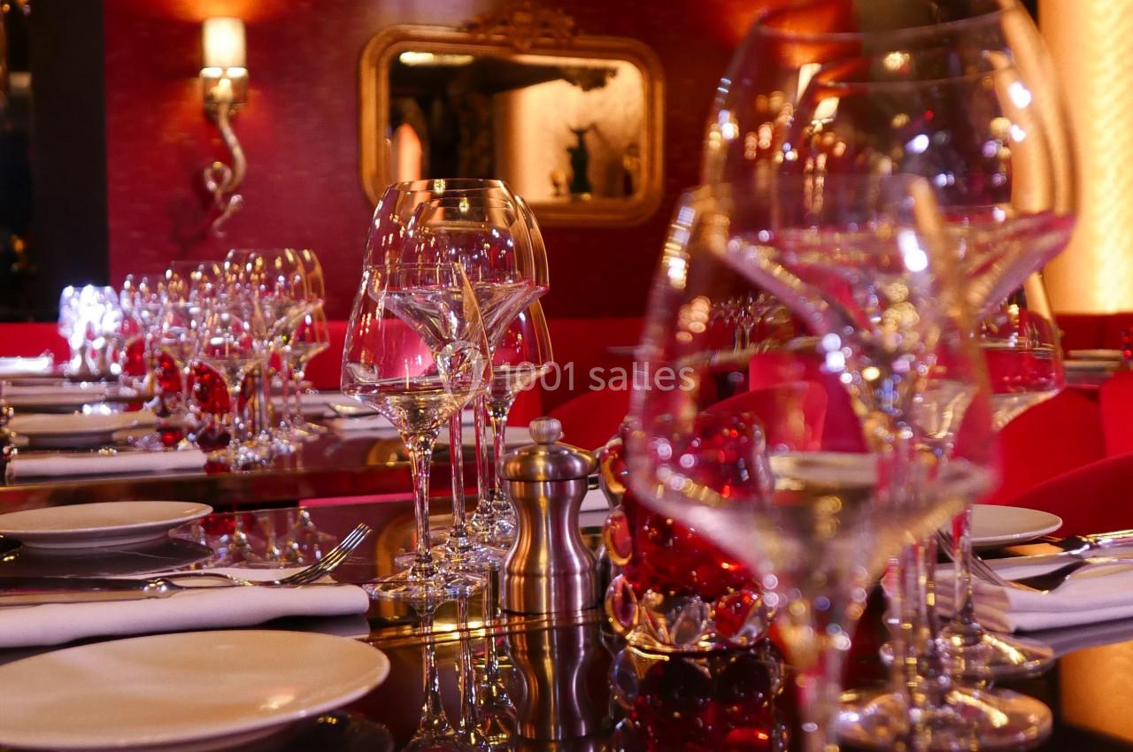 Table élégamment dressée avec des verres à vin, des couverts et des décorations rouges dans un restaurant chaleureux.