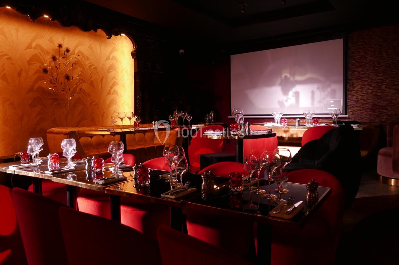 Salle de restaurant élégante avec tables dressées, chaises rouges et éclairage tamisé.