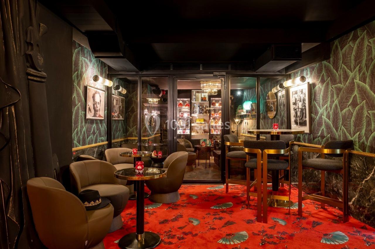 Salle de bar intimiste avec fauteuils, tables basses, tapis rouge à motifs et murs décorés de feuilles tropicales.