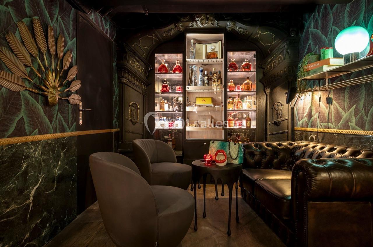 Salon élégant avec fauteuils, canapé en cuir, étagères éclairées contenant des bouteilles et décoration murale sophistiquée.