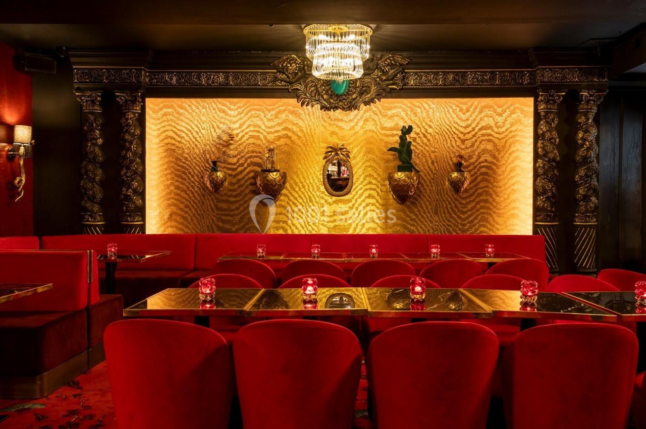 Salle de restaurant avec fauteuils rouges, tables dorées, murs texturés dorés et éclairage tamisé.