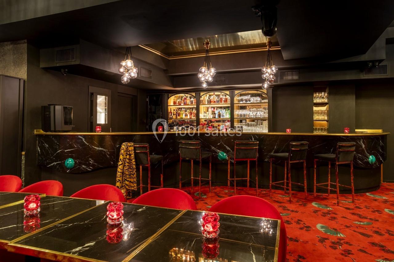 Bar élégant avec comptoir en marbre noir, tabourets hauts, éclairage tamisé et tables ornées de bougies rouges.