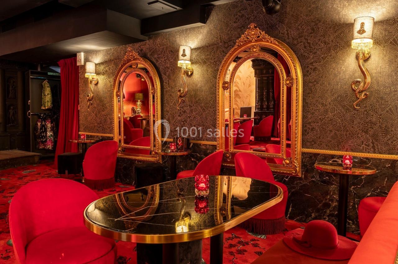 Salle élégante avec fauteuils rouges, tables en marbre noir, miroirs dorés et éclairage tamisé.