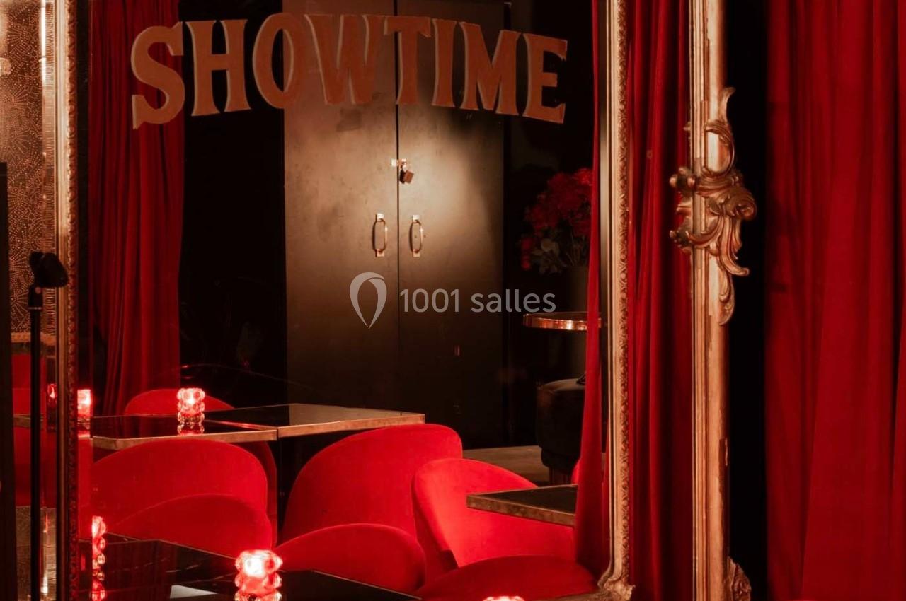 Miroir encadré doré reflétant des rideaux rouges, des sièges en velours et une inscription ’SHOWTIME’.