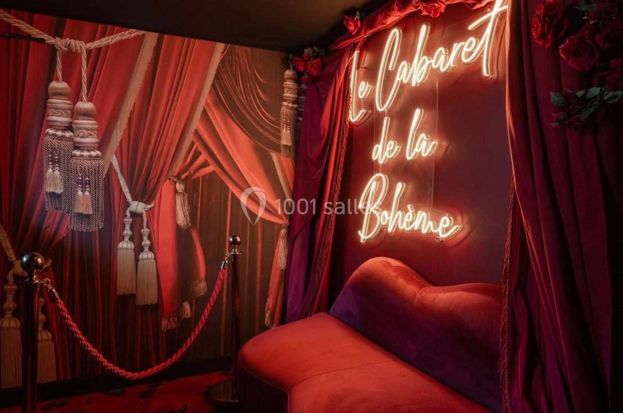 Espace décoré de rideaux rouges, canapé en velours et enseigne lumineuse indiquant ’Le Cabaret de la Bohème’.