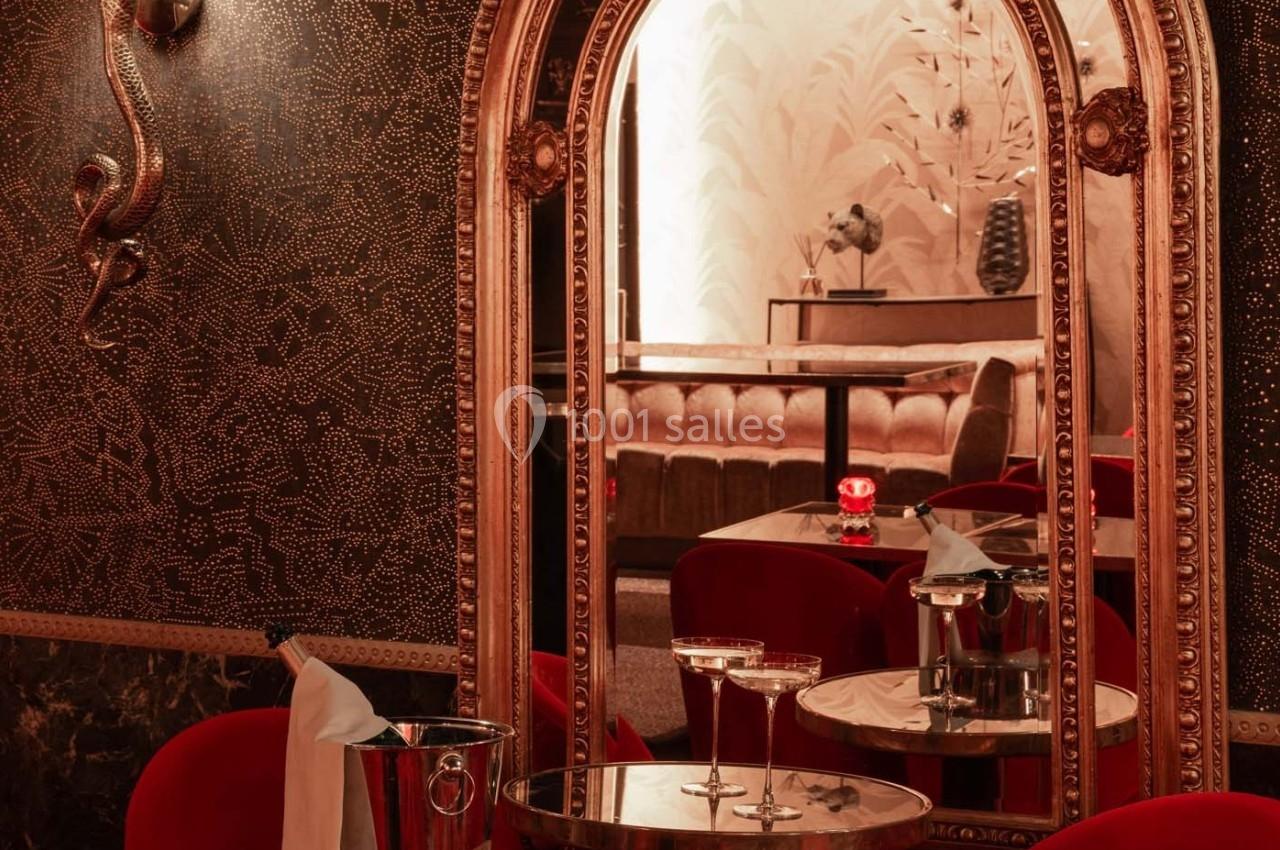 Un salon élégant avec des fauteuils rouges, des tables en miroir, un seau à champagne et une lumière tamisée.