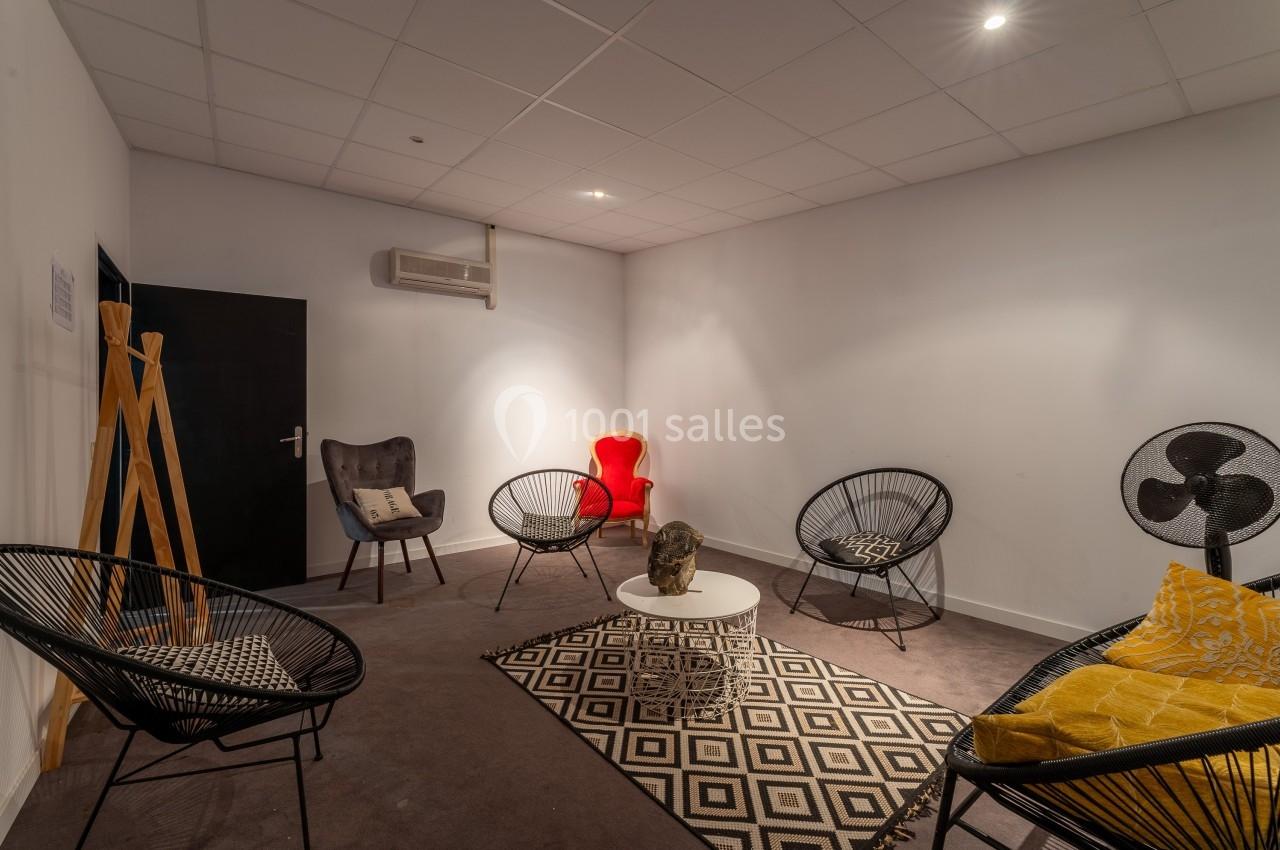Salle de détente avec fauteuils variés, table basse, tapis géométrique et éclairage tamisé.