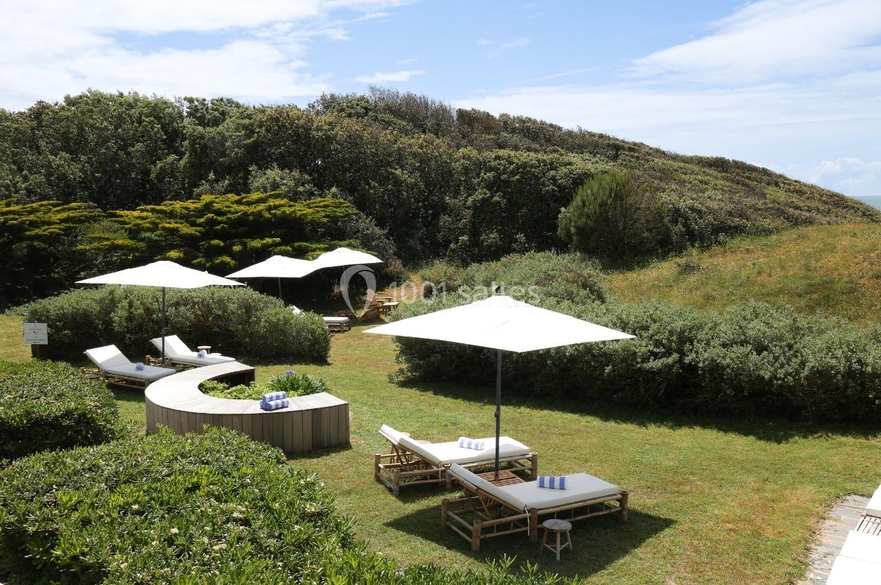 Chaises longues et parasols blancs disposés sur une pelouse entourée de végétation, sous un ciel partiellement dégagé.