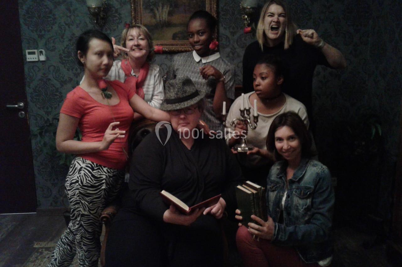Un groupe de personnes posant dans une pièce sombre avec des accessoires variés, comme des livres et un chandelier.