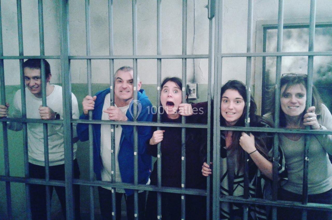 Cinq personnes souriantes ou expressives derrière des barreaux dans une mise en scène évoquant une prison.