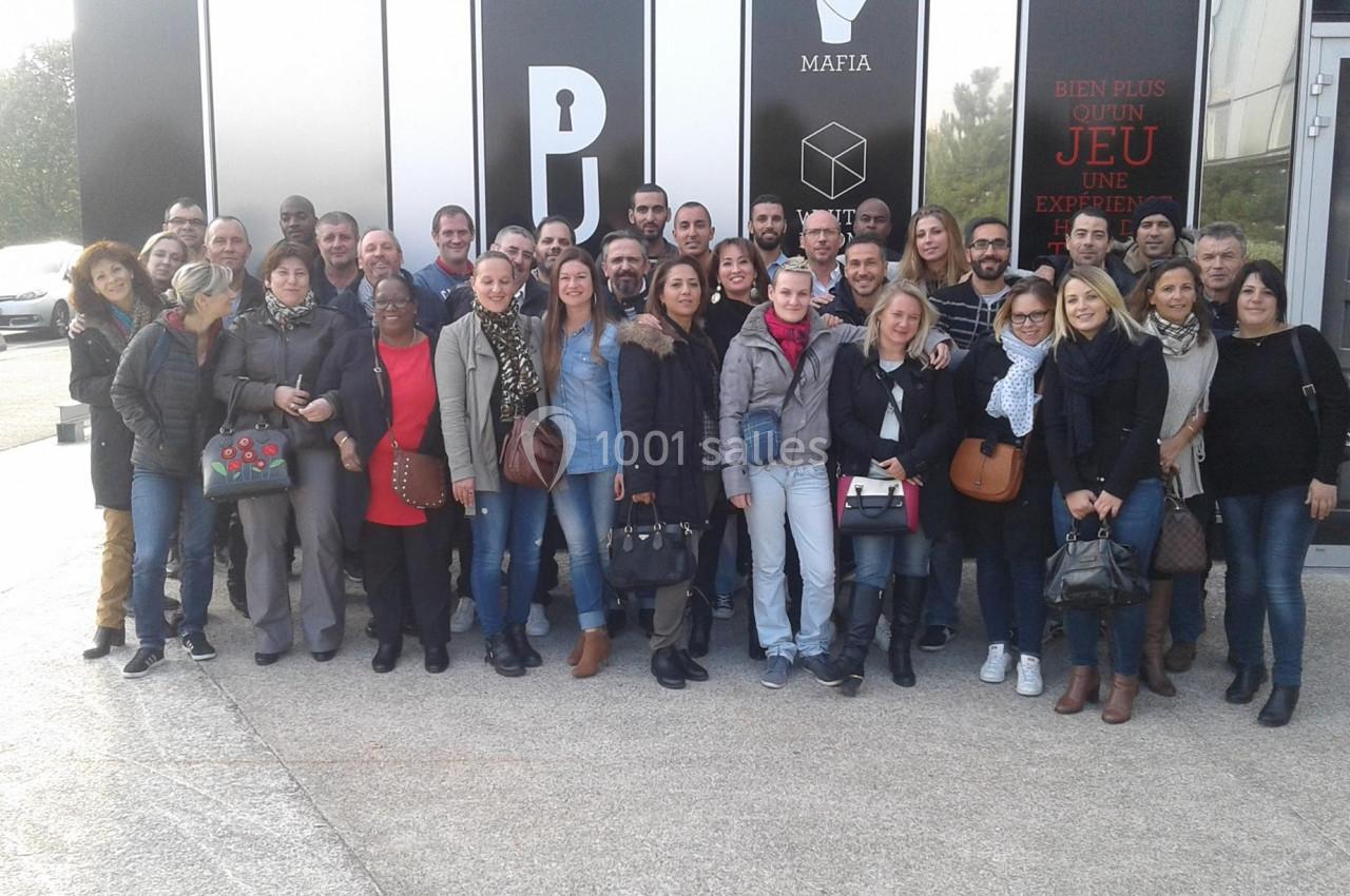 Un groupe de personnes pose devant un bâtiment avec des inscriptions sur la façade.