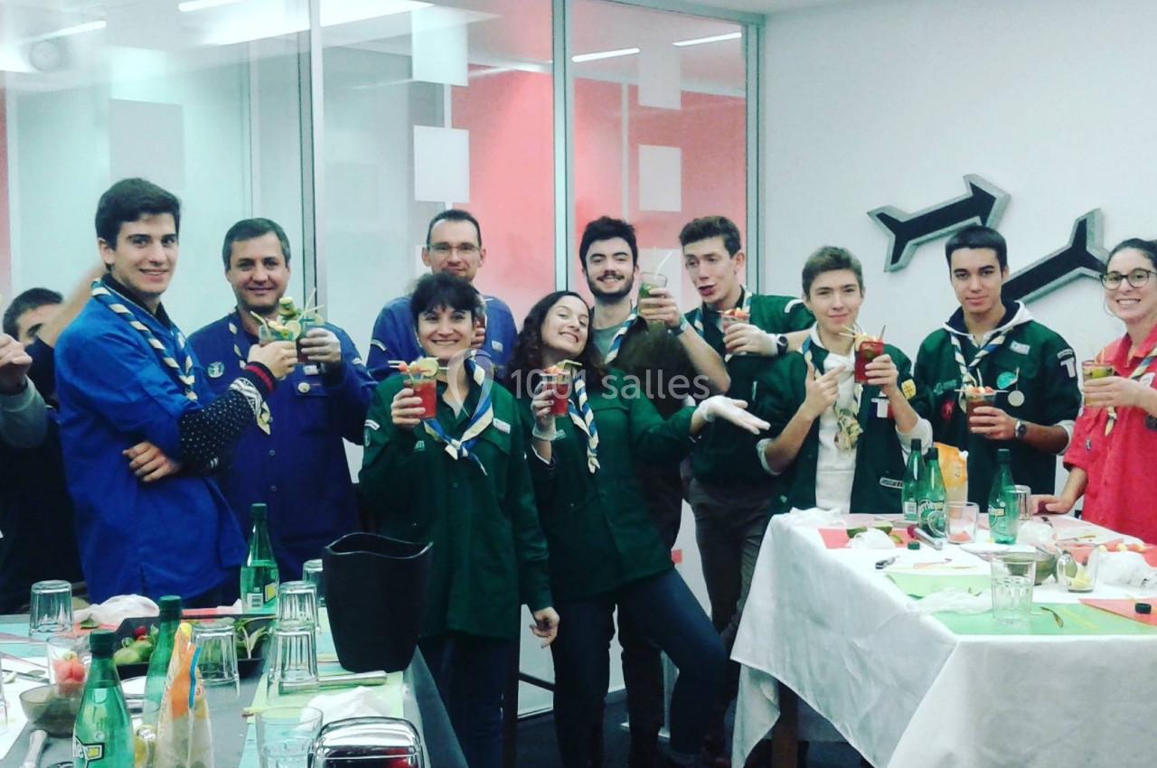 Un groupe de personnes en tenue de scouts partage un moment convivial autour de boissons dans une salle lumineuse.