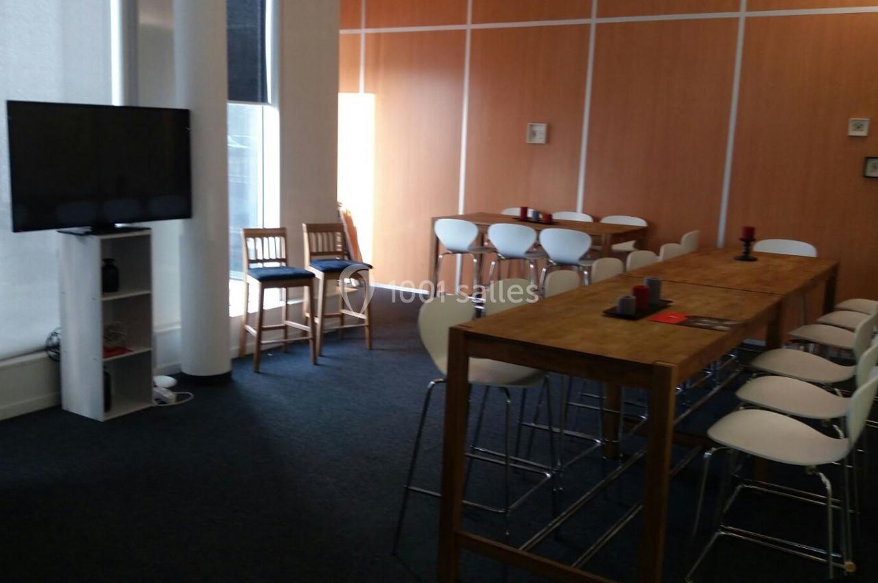 Salle de réunion lumineuse avec table haute, chaises blanches, écran TV et murs en bois clair.